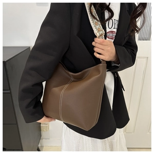 Detail of brown lychee leather bucket bag with white contrast stitching and jacquard strap