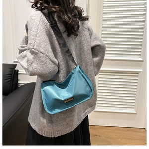 Detailed back view of a teal nylon crossbody bag featuring a wide adjustable strap on a model