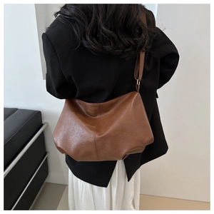Detail of vintage brown leather dumpling bag showing natural pleats and wide strap on model
