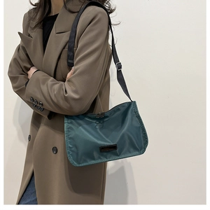 Detail of teal nylon crossbody bag with adjustable strap worn by model against a white wall