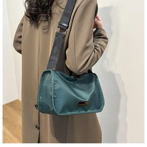 Minimalist dark green nylon crossbody bag with wide shoulder strap worn by a model