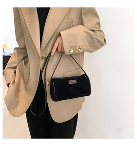 Dettaglio di una borsa baguette a cilindro in camoscio nero con logo dorato e tracolla
