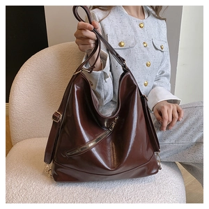Detail of deep brown glossy leather tote bag with gold hardware and zipper accents