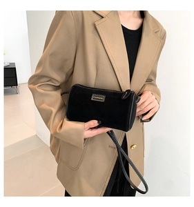 Dettaglio borsa baguette in camoscio nero con placca dorata tenuta da modella in blazer marrone