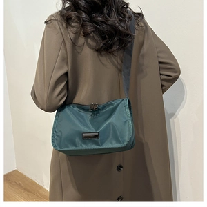 Detail of dark green nylon crossbody bag showing wide black strap and dual metal zippers