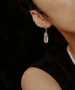 Close-up of a silver teardrop earring with white cat eye stone on a model's ear
