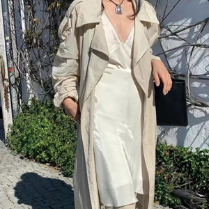 Gros plan d'un collier à pendentif carré mat porté avec un trench beige et une robe satin
