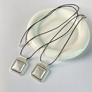 Collier rétro avec pendentif carré argenté mat et cordon noir sur une assiette