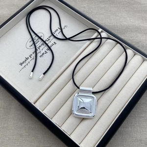 Collier à pendentif géométrique argenté avec cordon noir sur présentoir en velours