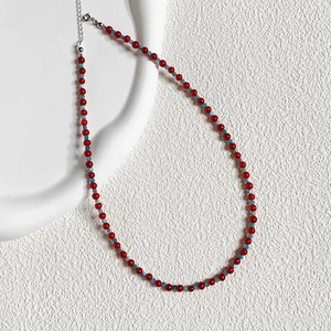 Collier minimaliste en perles d'agate rouge avec accents bleus sur plateau blanc