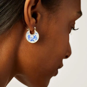 Close-up of blue and white enamel hoop earrings on model with porcelain design