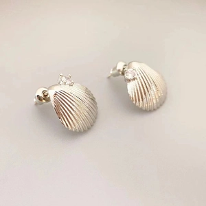 Macro detail of shell-shaped silver earring featuring a centered sparkling zircon stone