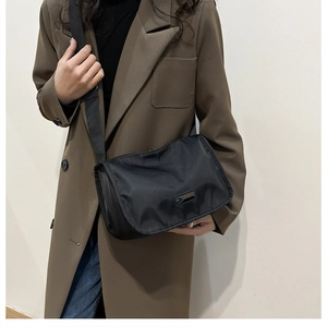 Detail of a lightweight black nylon crossbody bag with wide shoulder strap worn by model
