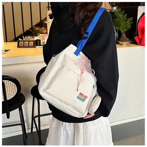 Detail of canvas bucket bag showing blue straps, pink drawstring and embroidered patches