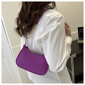 Detail of purple felt underarm bag with V-shaped quilting and gold chain strap on model