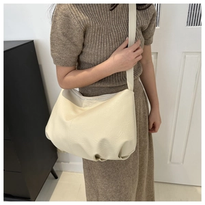 Detailaufnahme einer cremefarbenen Faltenhandtasche aus PU-Leder, getragen von einem Modell