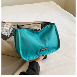Detail of teal nylon shoulder bag showing sleek metallic plaque and smooth fabric texture