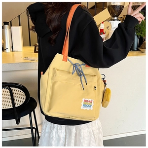 Detail of yellow tote bag with orange handles, blue drawstring, and embroidered WAAII patch