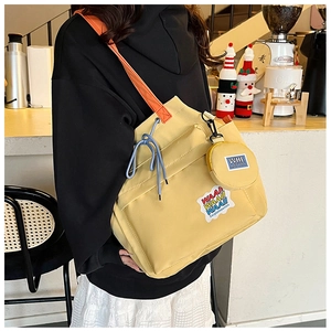 Detail of yellow canvas bucket bag with orange strap and rainbow lettering in a cafe setting