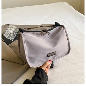 Close-up of light grey nylon crossbody bag with dual metal zippers and texture detail