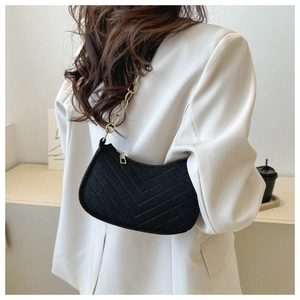 Detail of black chevron quilted felt baguette bag with golden chain on white blazer