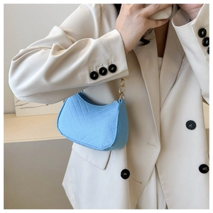 Detail of light blue quilted felt underarm bag with gold chain strap on beige blazer