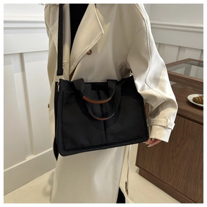 Détail du grand cabas en toile noire avec deux poches et finitions en cuir marron