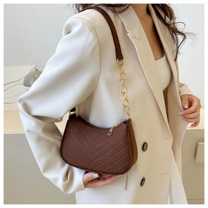 Brown quilted felt underarm bag with gold chain strap on a model wearing white suit