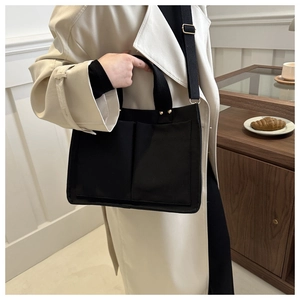 Détail du sac cabas en toile noire montrant les poches avant et les sangles métalliques