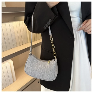 Detailed view of grey felt underarm bag featuring gold chain strap in a library setting