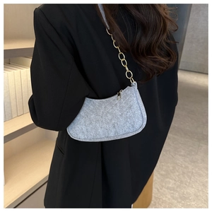 Close-up of grey quilted felt crescent shoulder bag with golden chain strap on model