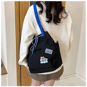 Back view of a black canvas tote bag with blue straps and mini pouch on model
