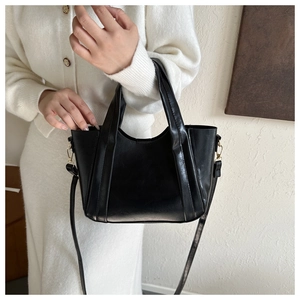 Detail of black faux leather tote bag with gold metal buckles and detachable shoulder strap