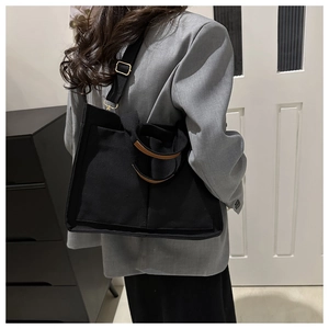 Sac fourre-tout en toile noire avec poignées marron porté par un mannequin élégant
