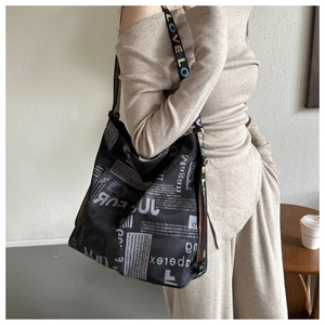 Detailweergave van zwarte canvas tas met retro krantenprint en kleurrijke love-riem
