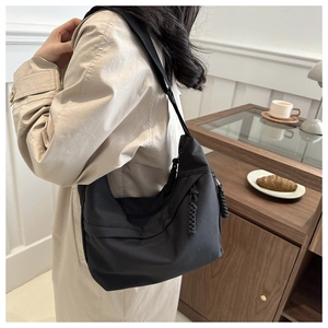 Detail of black nylon crescent bag with textured woven rope zipper on a trench coat