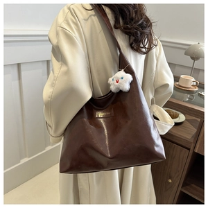 Detail of dark brown glossy tote bag with fashion label and white cloud plush charm
