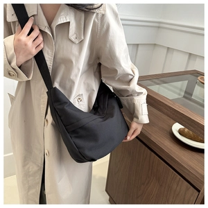 Close-up of black nylon crescent shoulder bag on beige trench coat for winter style