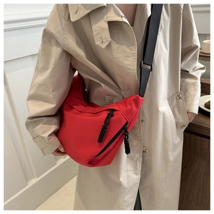 Detail of red crescent bag with adjustable black strap worn over a beige trench coat