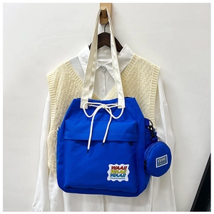 Detail of blue canvas bucket bag with letter patches, drawstring closure and wide strap