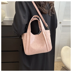 Model wearing a dusty rose tote bag in matte leather over a black wool coat