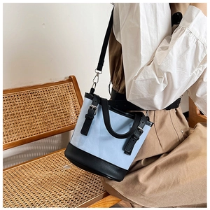 Detail of light blue bucket bag with black leather straps and metal buckle details