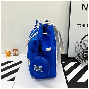 Detail of bright blue canvas bucket bag with white handles and round coin purse attachment