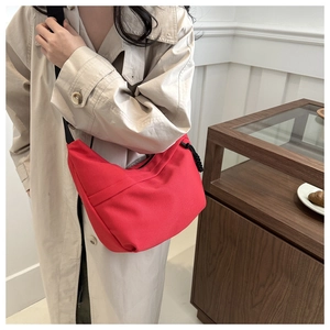 Detail of red crescent canvas crossbody bag with black strap worn by a female model