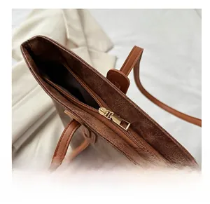 Close-up of smooth gold metal zipper on brown textured leather tote bag detail