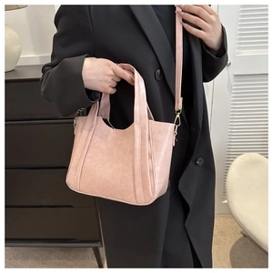 Light pink faux leather tote bag detail with gold hardware on black coat background