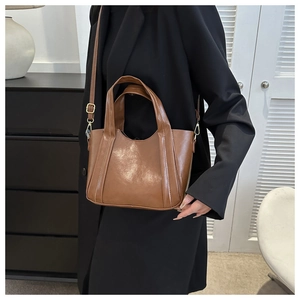 Brown oil leather tote bag with dual handles and gold buckles shown on a female model