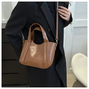 Brown oil leather tote bag with gold metal buckle detail shown on a black suit blazer