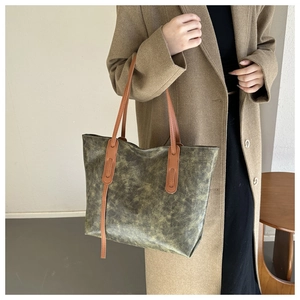 Detail of vintage olive green tote bag with brown leather handles worn by a model
