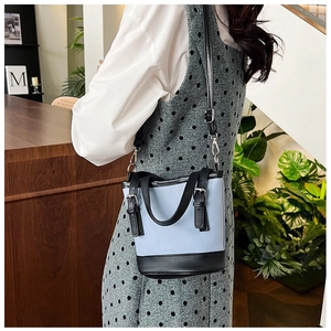 Detail of a two-tone denim bucket bag with black leather straps shown in a lifestyle setting